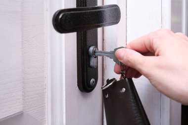 Anahtarı tutan bir el, beyaz ahşap bir kapıyı açmak ya da kilitlemek için bir anahtar deliğine sokar. Ev güvenliği ve koruma kavramı..