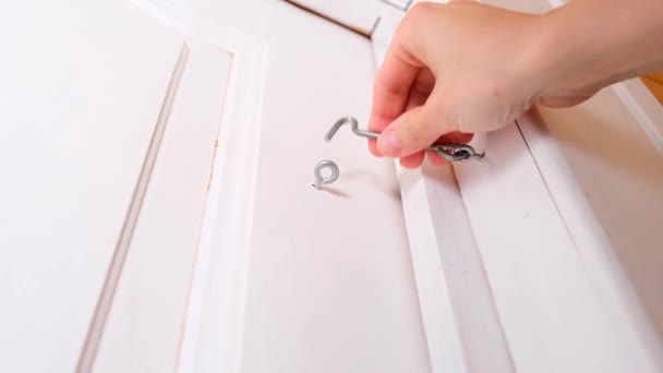 Una mano desbloqueando un gancho de puerta y abriendo la puerta de madera blanca, luego cerrándola y bloqueándola de nuevo, dispositivo simple para la seguridad y protección de la casa — Vídeo de stock