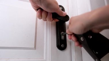 Sığmak için çırpınan bir el, anahtar deliğine bir anahtar yerleştirir ve onu beyaz ahşap bir kapıyı, ev güvenliğini ve korunma konseptini kilitlemek için çevirir.