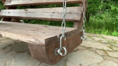 Büyük ahşap salıncak, boş koltuk yazın bir köye gidip geliyor, arka planda yeşil yapraklar, nostalji ve melankolik manzara.