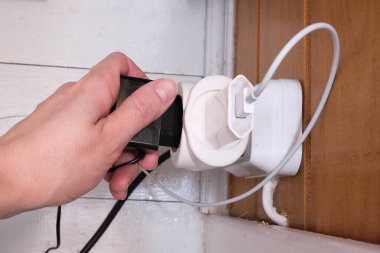 Uzantısı olan aşırı yüklenmiş prizler ve prizlere takılı bir sürü priz prizin prizine takılan bir el, ahşap bir evde yangın ve kısa devre riski.