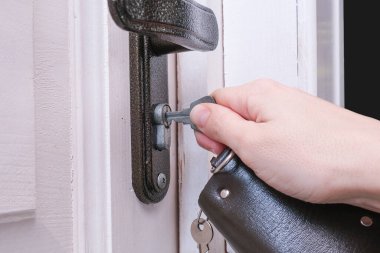 Anahtarı tutan bir el, beyaz ahşap bir kapıyı açmak ya da kilitlemek için bir anahtar deliğine sokar. Ev güvenliği ve koruma kavramı..
