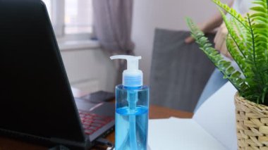 Bulanık yüzlü kadın maske takıyor. Evde dizüstü bilgisayarda çalışıyor. Koruyucu olarak el dezenfektanı var.
