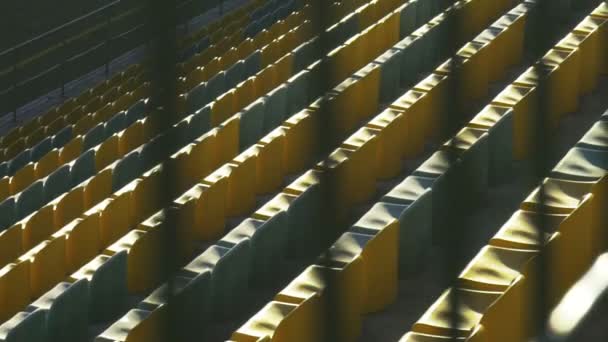 Sillas amarillas en un estadio vacío detrás de una valla de metal, cámara lenta 120fps — Vídeo de stock