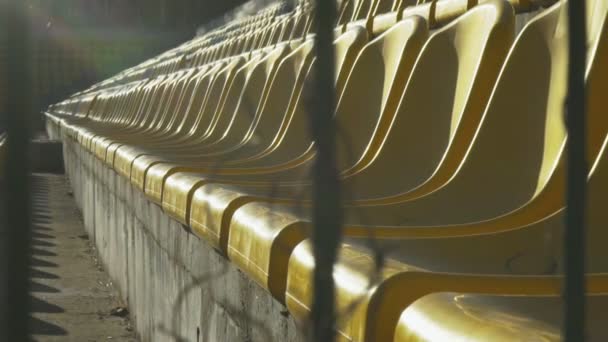 Желтые стулья на пустом стадионе за металлическим забором, замедленная съемка 120 кадров в секунду — стоковое видео