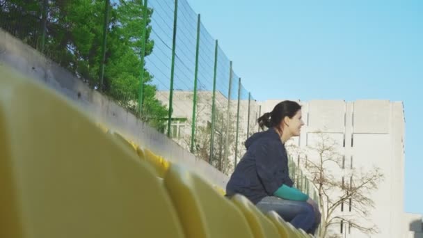 Одна девушка сидит на трибуне стадиона, 4k — стоковое видео