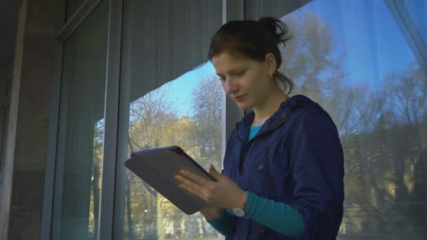 Μια νεαρή γυναίκα με ένα δισκίο στο παράθυρο του σπιτιού, 4k — Αρχείο Βίντεο