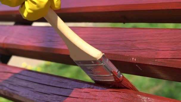 Close-up van de hand in gele beschermende handschoen schilderen houten plank met penseel borstel in rode kleur, slow-motion — Stockvideo