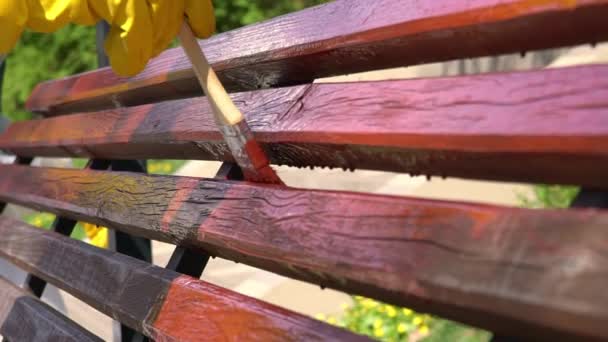 Close-up van de hand in gele beschermende handschoen schilderen houten plank met penseel borstel in rode kleur, slow-motion — Stockvideo