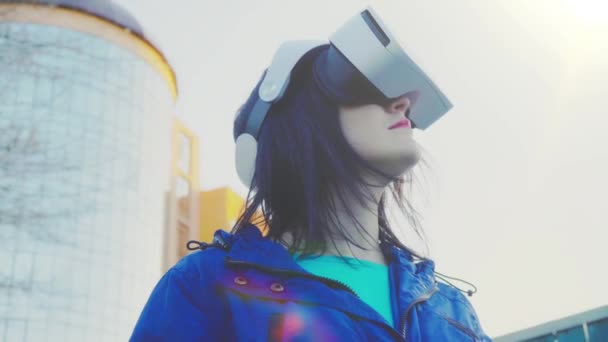 Mujer joven con gafas VR, auriculares, juegos virtuales y viendo videos al aire libre contra el fondo de un edificio de vidrio — Vídeos de Stock