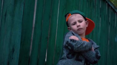 Küçük çocuk çocuk eski ahşap çit, Cap tarafından değişiklikleri yüz ifadeleri, serin 5 yaşındaki çocuk ayakta dik çocuk portresi yakınındaki kamera poz