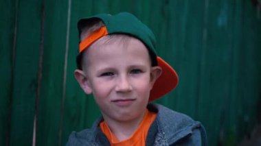 Küçük çocuk çocuk eski ahşap çit, Cap tarafından değişiklikleri yüz ifadeleri, serin 5 yaşındaki çocuk ayakta dik çocuk portresi yakınındaki kamera poz