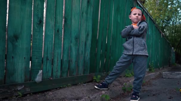 小男孩摆在相机旁边的老木栅栏 一个陡峭的男孩的肖像站在 孩子改变面部表情 凉爽5岁的孩子 — 图库视频影像