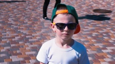 Genç çocuk güneş gözlüğü ve yürüme, ağır çekim çocuk 6 yaşında bir çocuk, sokakta yürürken bir kap içinde