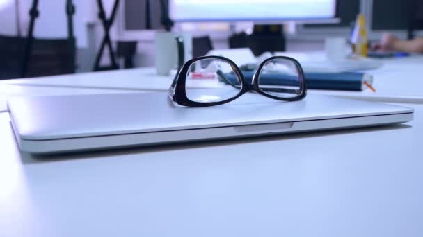 Окуляри лежать на ноутбуці на офісному столі, крупним планом — стокове відео