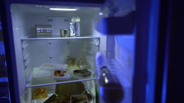 冷蔵庫で食べ物を探している男 彼の手にビールのボトルを持つUnshaven男は冷蔵庫で食用何かを探しています 夜の飢え ハンガー 学士の冷蔵庫に古い食べ物がいっぱい — ストック動画