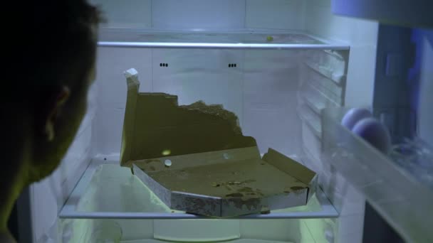 冷蔵庫で食べ物を探している男 Unshaven男は彼の冷蔵庫で掘る 彼はピザを取ります 夜の飢え ハンガー 学士号の冷蔵庫後ろからの眺め 古い食べ物でいっぱいの汚れた冷蔵庫 隔離だ — ストック動画