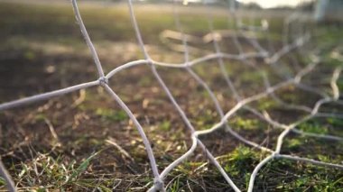 Futbol golü. Top kaleye doğru uçuyor. Futbolcu gol attı. Şebekeye yakın çekim. Eski futbol sahası. Sokak sporu. Çocuk Oyunu. Güneş parlıyor.