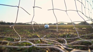 Yırtık bir futbol ağının yakın çekimi. Futbol topu ağdan geçiyor. Eski bir futbol sahası. Sokak sporu. Çocuk Oyunu. Güneş ızgaranın içinden parlıyor. Kriz. Futbol mu?.