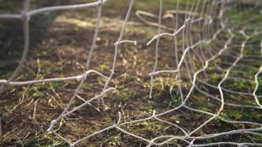 Yırtık bir futbol ağının yakın çekimi. Futbol topu ağdan geçiyor. Eski bir futbol sahası. Sokak sporu. Çocuk Oyunu. Güneş ızgaranın içinden parlıyor. Kriz. Futbol mu?.