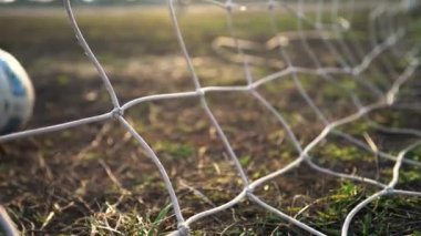 Futbol golü. Top kaleye doğru uçuyor. Futbolcu gol attı. Şebekeye yakın çekim. Eski futbol sahası. Sokak sporu. Çocuk Oyunu. Güneş parlıyor.