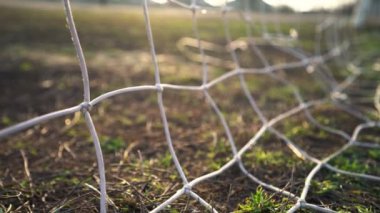 Futbol golü. Top kaleye doğru uçuyor. Futbolcu gol attı. Şebekeye yakın çekim. Eski futbol sahası. Sokak sporu. Çocuk Oyunu. Güneş parlıyor.