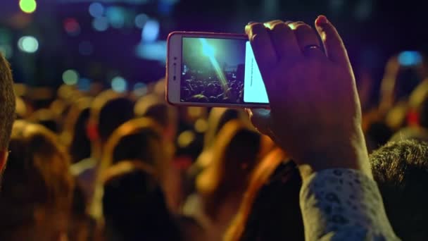 免费音乐会 快乐的人们正在观看一场令人惊奇的音乐会 快乐的歌迷跳起来 举起他们的手 粉丝们正在用智能手机拍摄一场音乐会 现场音乐会 — 图库视频影像