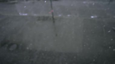 Kar taneleri gri asfalta düşer, manzaranın üstüne. İlk kar yağışı. Kaldırıma kar yağar. Kış havası. Soyut doğal arkaplan, hareket halindeki beyaz parçacıklar. 