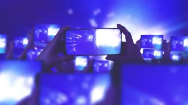 Kalabalık bir konser izliyor, şarkı söylüyor, zıplıyor. Çarpıcı sahne ışıkları. Mutlu insanlar. Müzik konsepti. Hayranlar akıllı telefonlardan video kaydediyor. Bir sürü akıllı telefon. Canlı yayın. Hikayeler.