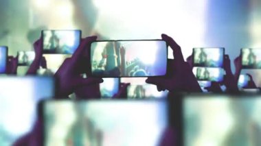 Hayranlar akıllı telefonlardan video kaydediyor. Bir sürü akıllı telefon. Canlı yayın. Hikayeler. Kalabalık bir konser izliyor, şarkı söylüyor, zıplıyor. Çarpıcı sahne ışıkları. Mutlu insanlar. Müzik konsepti.