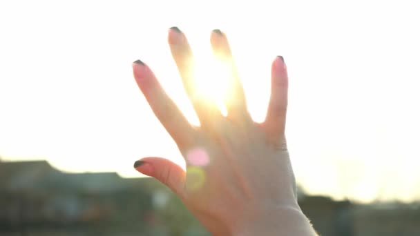 女性は手を通して明るい太陽を見る 太陽の魔法の光線はあなたの指を通して輝きます 幻想的な明るい光 フラッシュだ 太陽の下で日光浴をする女性 気をつけて 幸せよ — ストック動画