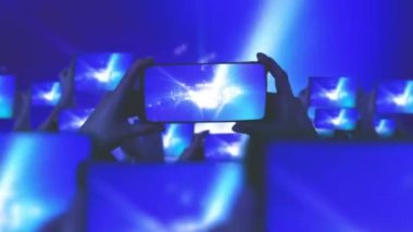 Konserdeki mutlu insanlar. Bir sürü akıllı telefon. Hayranlar akıllı telefonlardan video kaydediyor. Müzik konsepti. Canlı yayın. Hikayeler. Kalabalık bir konser izliyor, şarkı söylüyor, zıplıyor. Çarpıcı sahne ışıkları. 