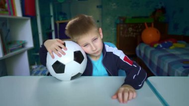 Üzgün çocuk masada futbol topuyla oturuyor. Karantina sırasında üzgün bir çocuk pencereden dışarı bakar. Çocuk arkadaşlarıyla futbol oynamayı hayal ediyor. Stadyumdaki maçın hasretini çekiyorum. Yalnızlık. 