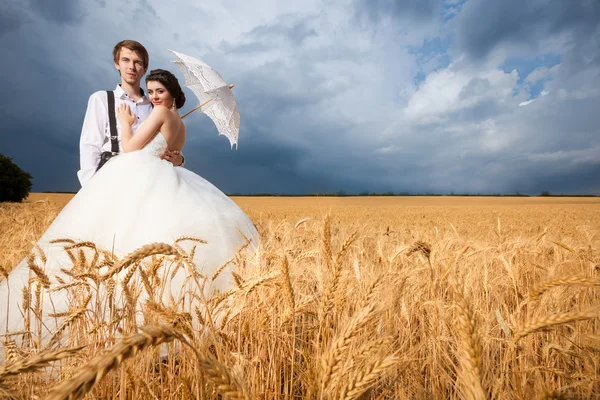 Gyönyörű fiatal menyasszony és a vőlegény a búzamező drámai ég — Stock Fotó