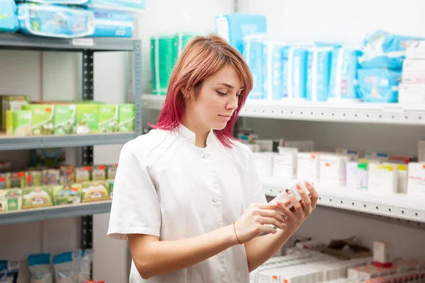 Female doctor in the drugstore looking at a box with pills — Stock Photo, Image