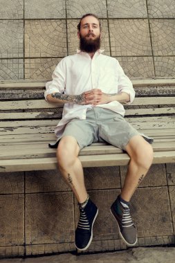 Serin görünümlü adam tatoos ile ve sandalyede oturan uzun sakal