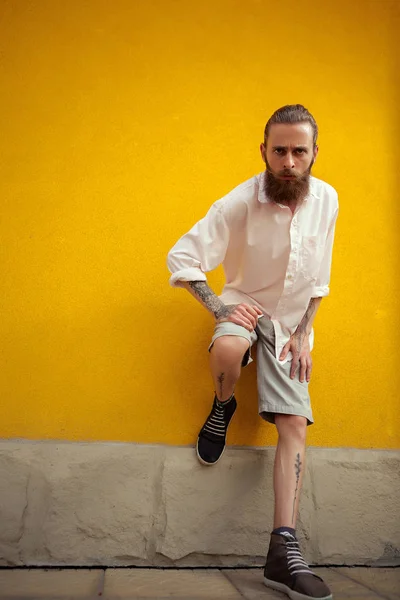 Szakállas és tetovált ember pózol a sárga fal — Stock Fotó