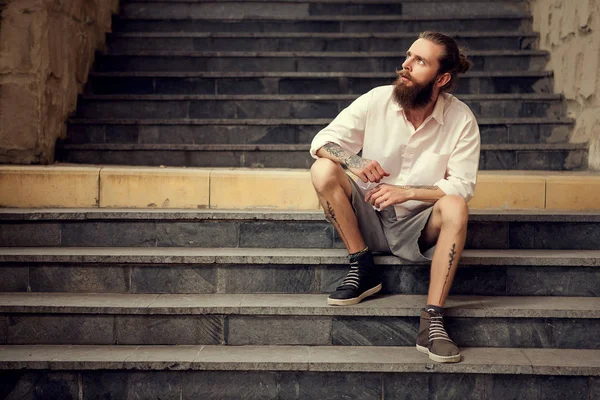 Beardead tatuado legal olhando cara sentado na rua em escadas — Fotografia de Stock