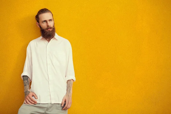 Bearded and tattooed hipster posing on yellow wall — Stock Photo, Image