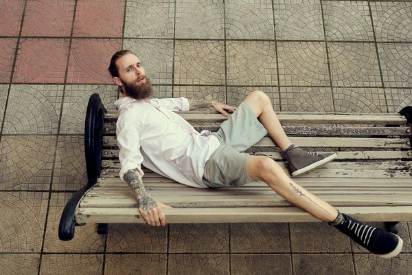 Barbudo tatuado deitado na cadeira e posando em estilo de moda — Fotografia de Stock