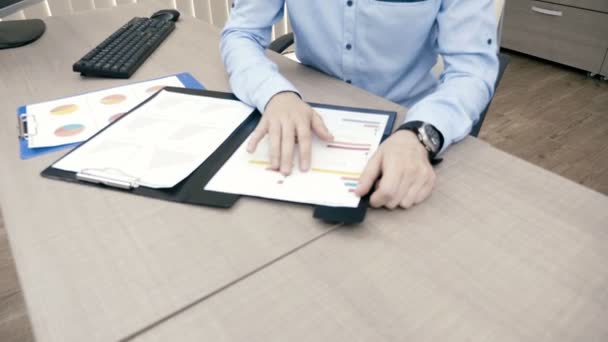 Pannen omhoog op zakenman werkt in zijn kantoor op de computer naast mappen gevuld met grafieken — Stockvideo