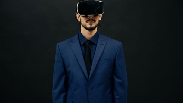 Чоловік у костюмі в гарнітурі VR на чорному студійному фоні відчуває віртуальну реальність — стокове відео