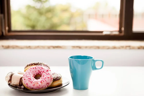 Donuts y una taza de café al lado del alféizar de la ventana — Foto de Stock