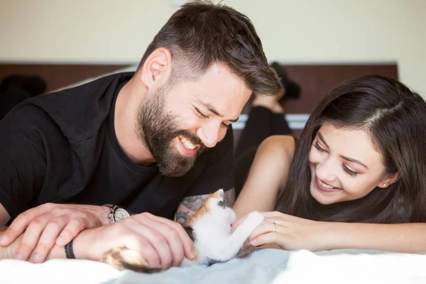 Красивая молодая влюбленная пара на кровати, играющая с котенком — стоковое фото