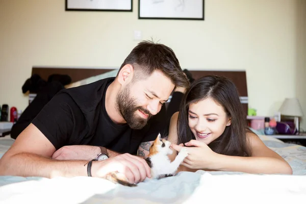 Beautiful young inlove couple on the bed playing with a kitten — Stock Photo, Image