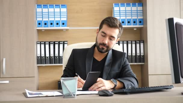 Jonge zakenman in zijn kantoor voor het maken van notities in een papieren notitieblok — Stockvideo