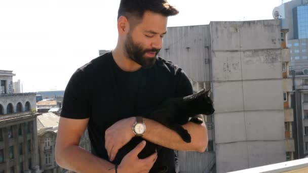 Vousatý bokovky chlap drží velké krásné černé kočky v ruce na terase — Stock video