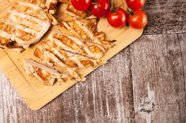 Domates yanındaki ahşap tahta üzerinde taze ızgara tavuk göğsü