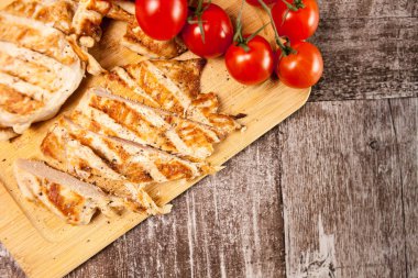 Domates yanındaki ahşap tahta üzerinde taze ızgara tavuk göğsü