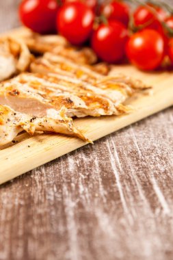 Domates yanındaki ahşap tahta üzerinde taze ızgara tavuk göğsü